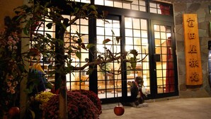 Un bâtiment traditionnel japonais, avec une enseigne en bois, une grande fenêtre et un pot de fleurs placé au premier plan.