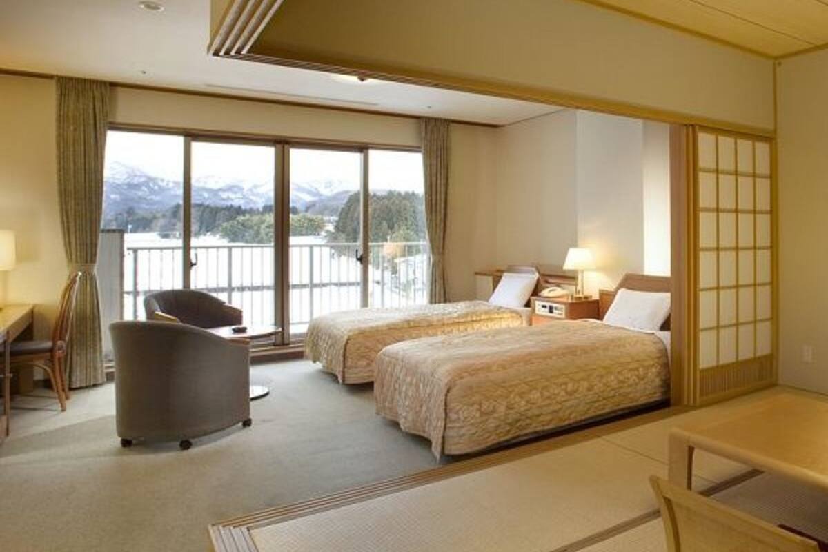 A hotel room with two beds, a desk, a chair, and a view of mountains through large windows.