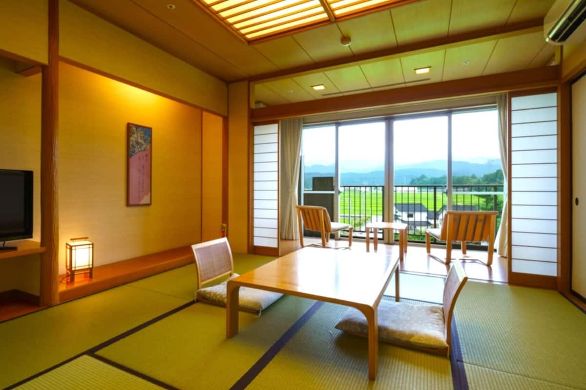 A traditional Japanese-style room with tatami flooring, a television, a table, and chairs.