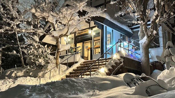 A snow-covered outdoor area with a staircase leading to a building with a blue facade. - Hotel Sejour mint (Hakuba)