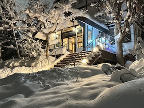 Un espacio exterior cubierto de nieve con una escalera que lleva a un edificio de fachada azul.
