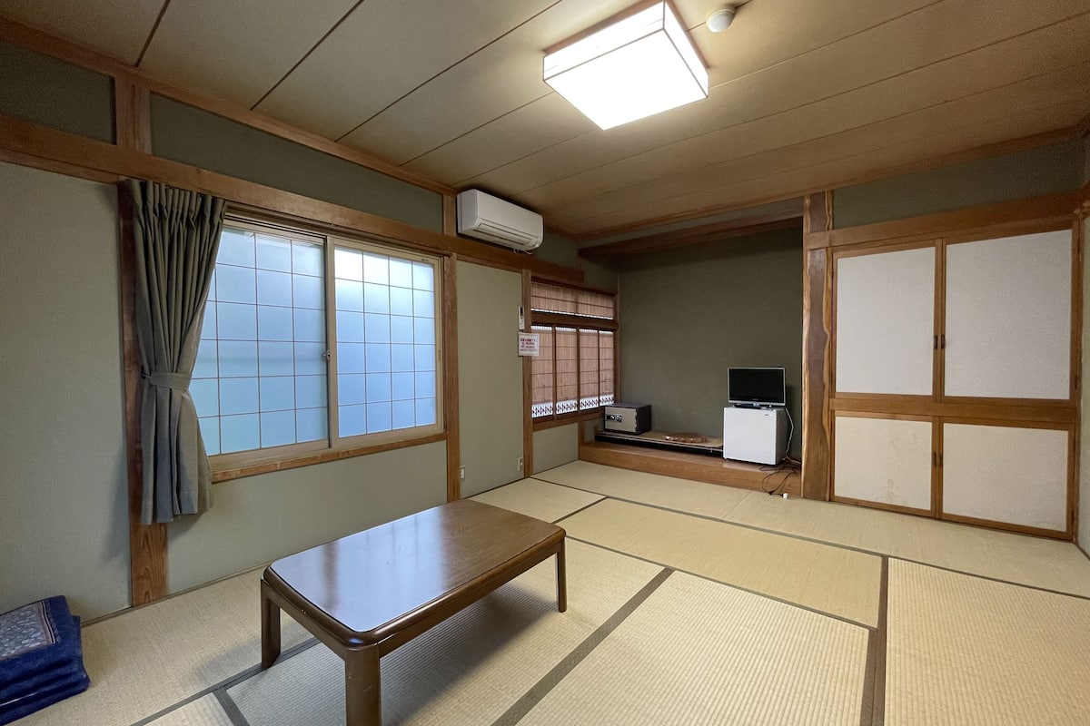 A traditional Japanese room with tatami flooring, a low wooden table, sliding doors, and a television.