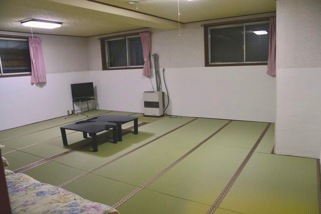 Ein Raum mit Tatami-Matten, einem Futon, einem Fernseher und einem Heizgerät.