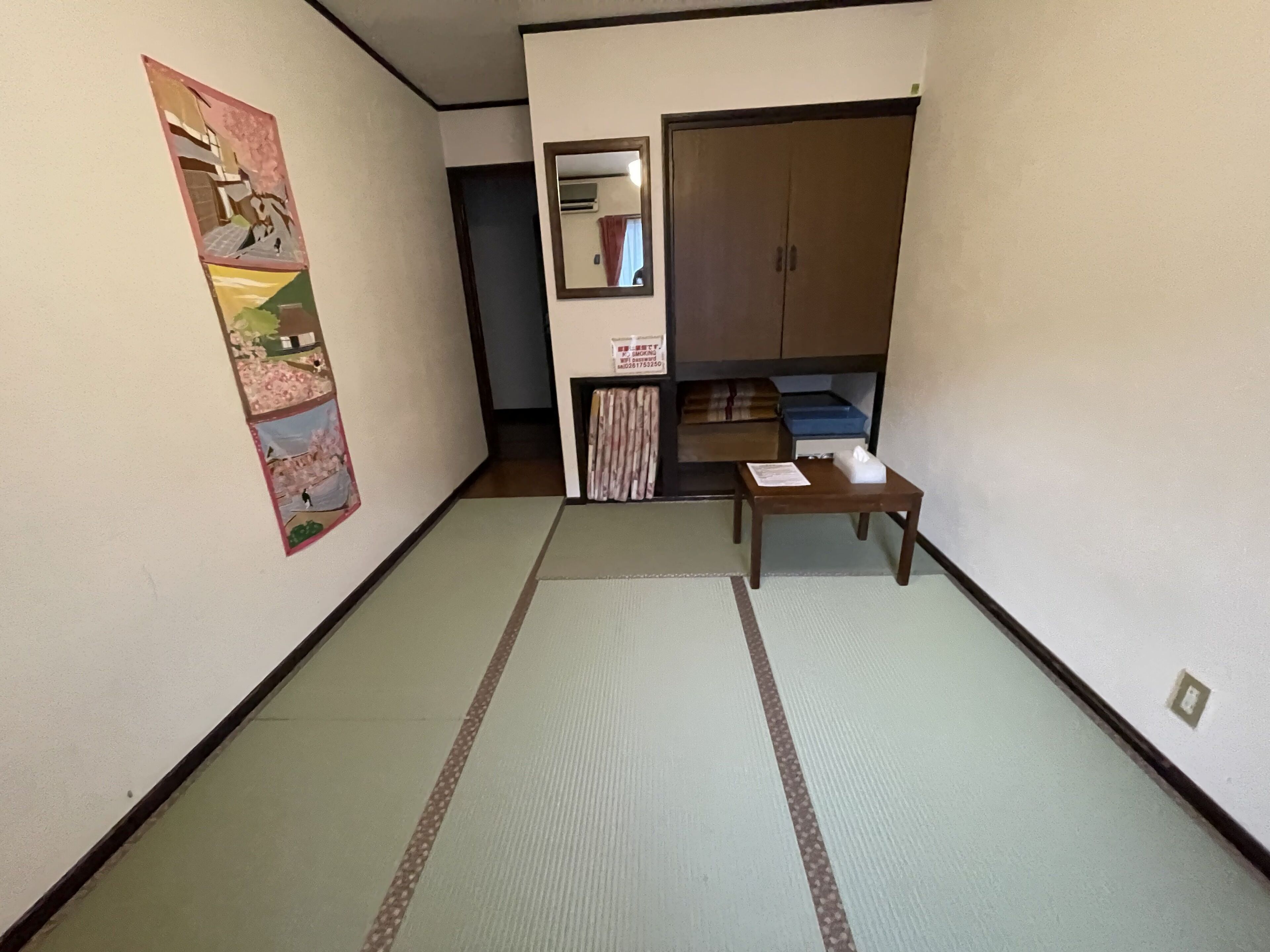 A room with tatami flooring, a wooden table, a cabinet, and a wall-mounted air conditioner.