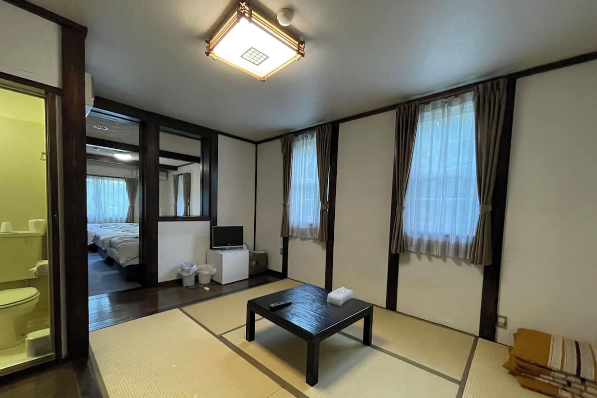 A traditional Japanese-style room with tatami flooring, a low table, a television, and a bed with a futon.