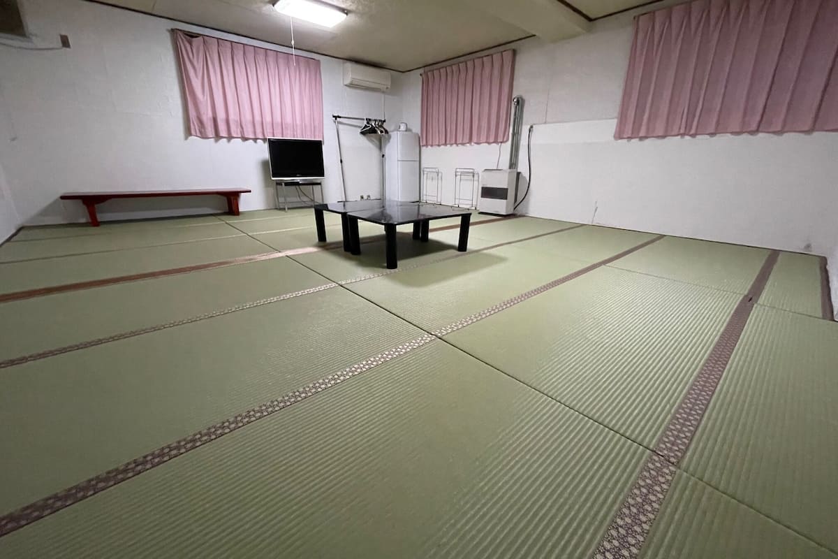 A tatami mat room with a low table, a bench, and a television.