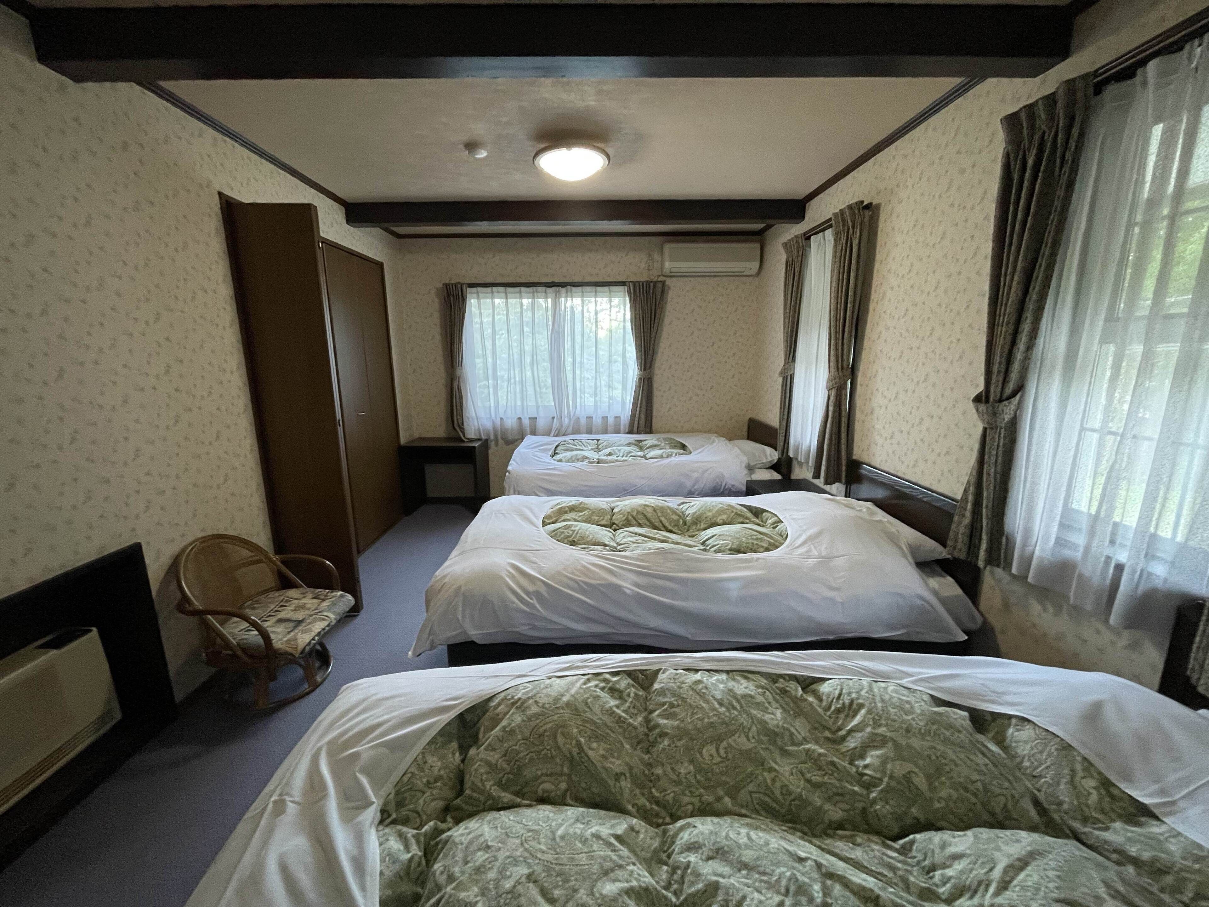 A hotel room with two beds, a small table, a chair, and a window with curtains.