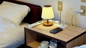 A neatly made hotel bed with white linens, a bedside table with a lamp, a phone, and a tray with two mugs. - Hotel Sejour mint (Hakuba)