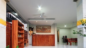 Un espace d’accueil avec un comptoir de réception en bois, un ventilateur de plafond et une grande œuvre d’art encadrée au mur.