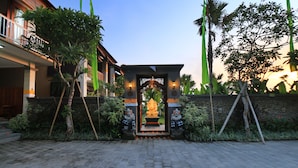 Une cour intérieure ornée d’une statue de Bouddha au centre, entourée de statues de pierre et de verdure.