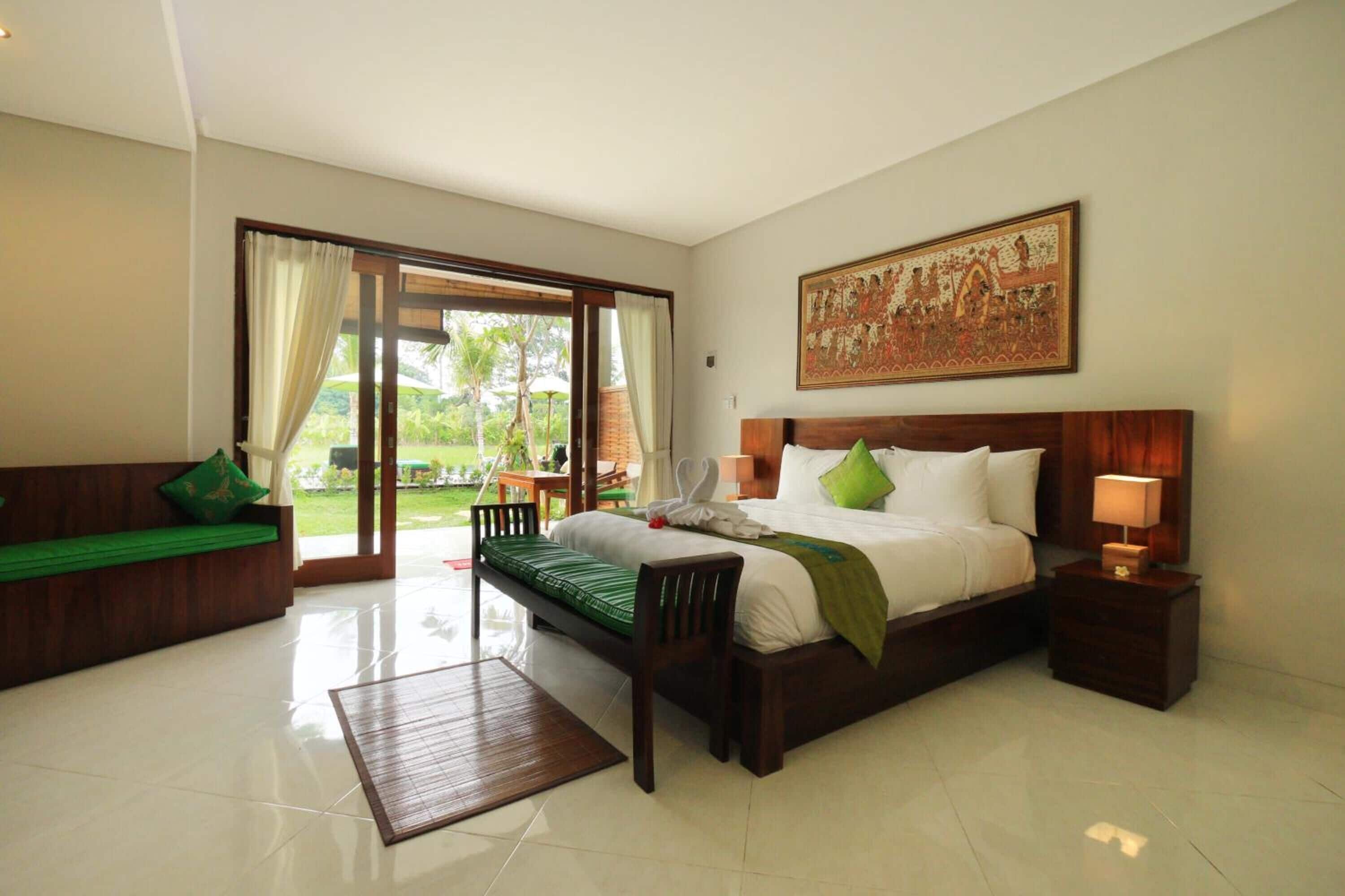 A spacious bedroom with a large bed, a wooden bench, and a view of the outdoors through a sliding door.