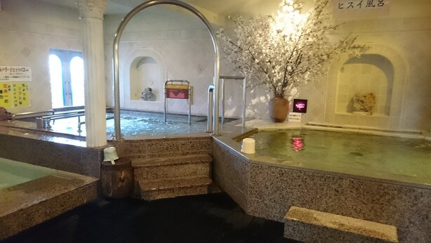 A traditional Japanese onsen with a stone bath, a wooden bench, and a sign indicating the water temperature. - Hiroshima Capsule Hotel & Sauna New Japan EX - Caters to Men (Hiroshima)