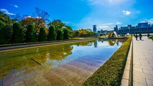 A reflective water feature in a park with a paved walkway, trees, and modern buildings in the background. - Hiroshima Capsule Hotel & Sauna New Japan EX - Caters to Men (Hiroshima)