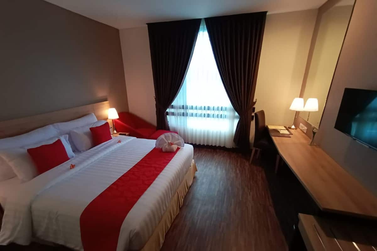 Een hotelkamer met een groot bed, een bureau, een stoel, een televisie en een raam met gordijnen.