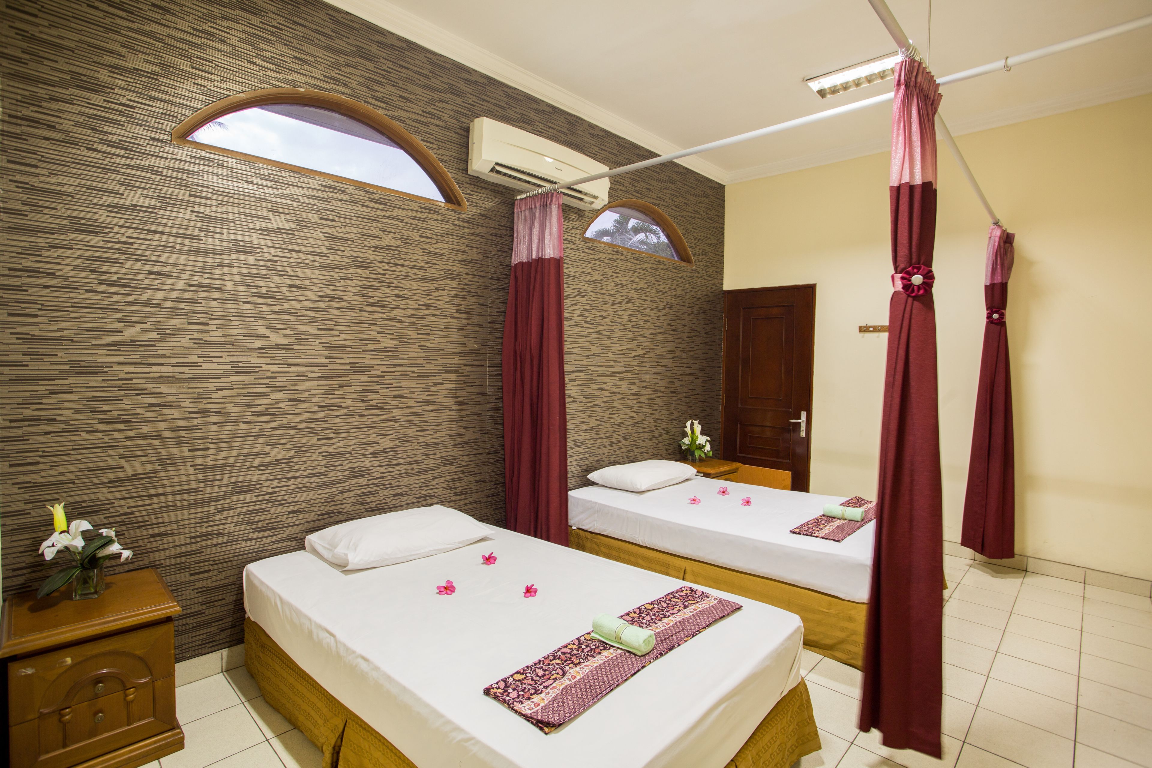 A hotel room with two beds, a wooden nightstand, a wall-mounted air conditioner, and a window with a curtain.