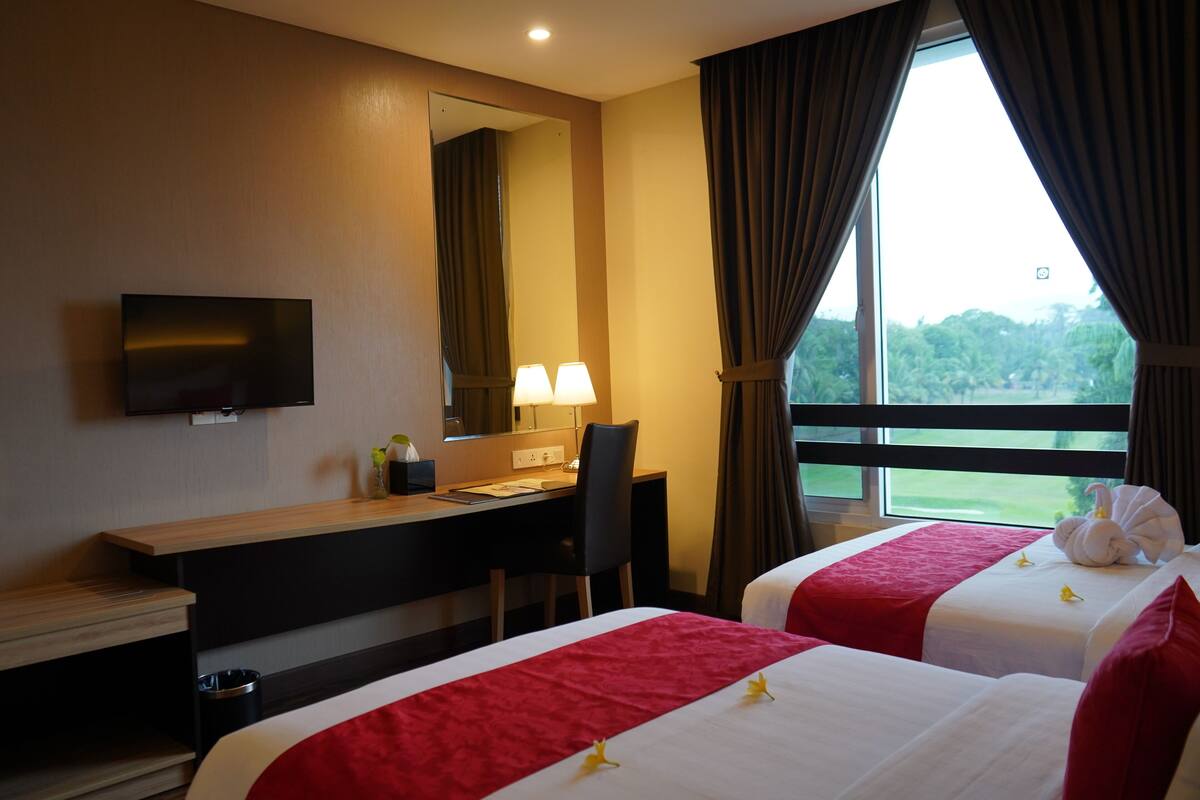 Een hotelkamer met twee bedden, een bureau, een televisie en een raam met gordijnen.