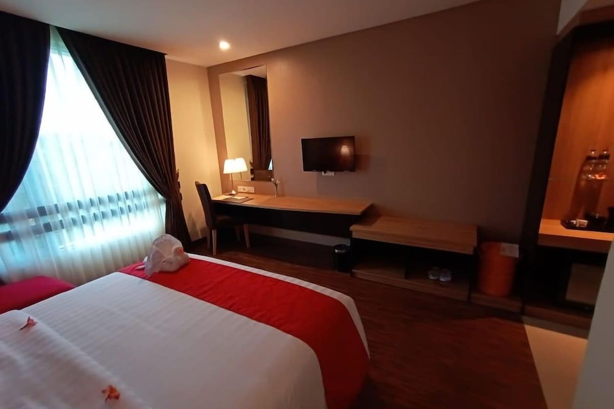 Une chambre d’hôtel avec un lit, un bureau, une chaise, une télévision et une fenêtre avec des rideaux.