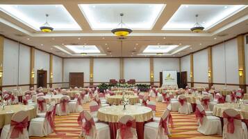 A large banquet hall with round tables, chairs, and a stage with floral arrangements.