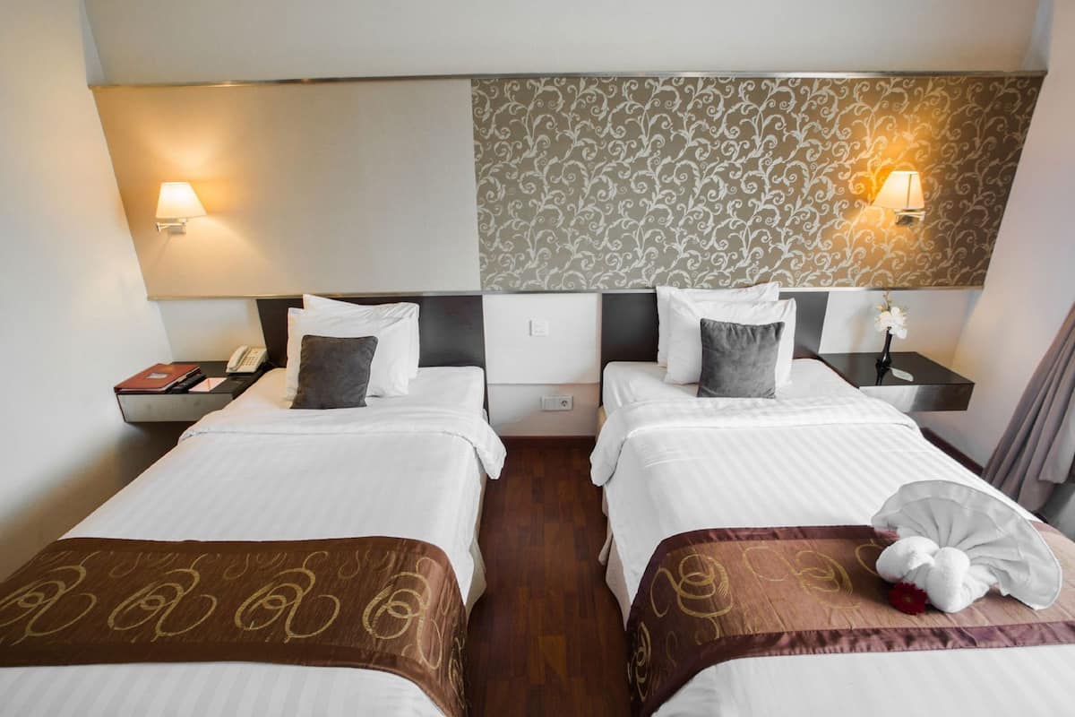 Een hotelkamer met twee bedden, een nachtkastje met een telefoon en een wandlamp.