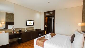 Habitación de hotel con cama, escritorio, espejo y televisión.