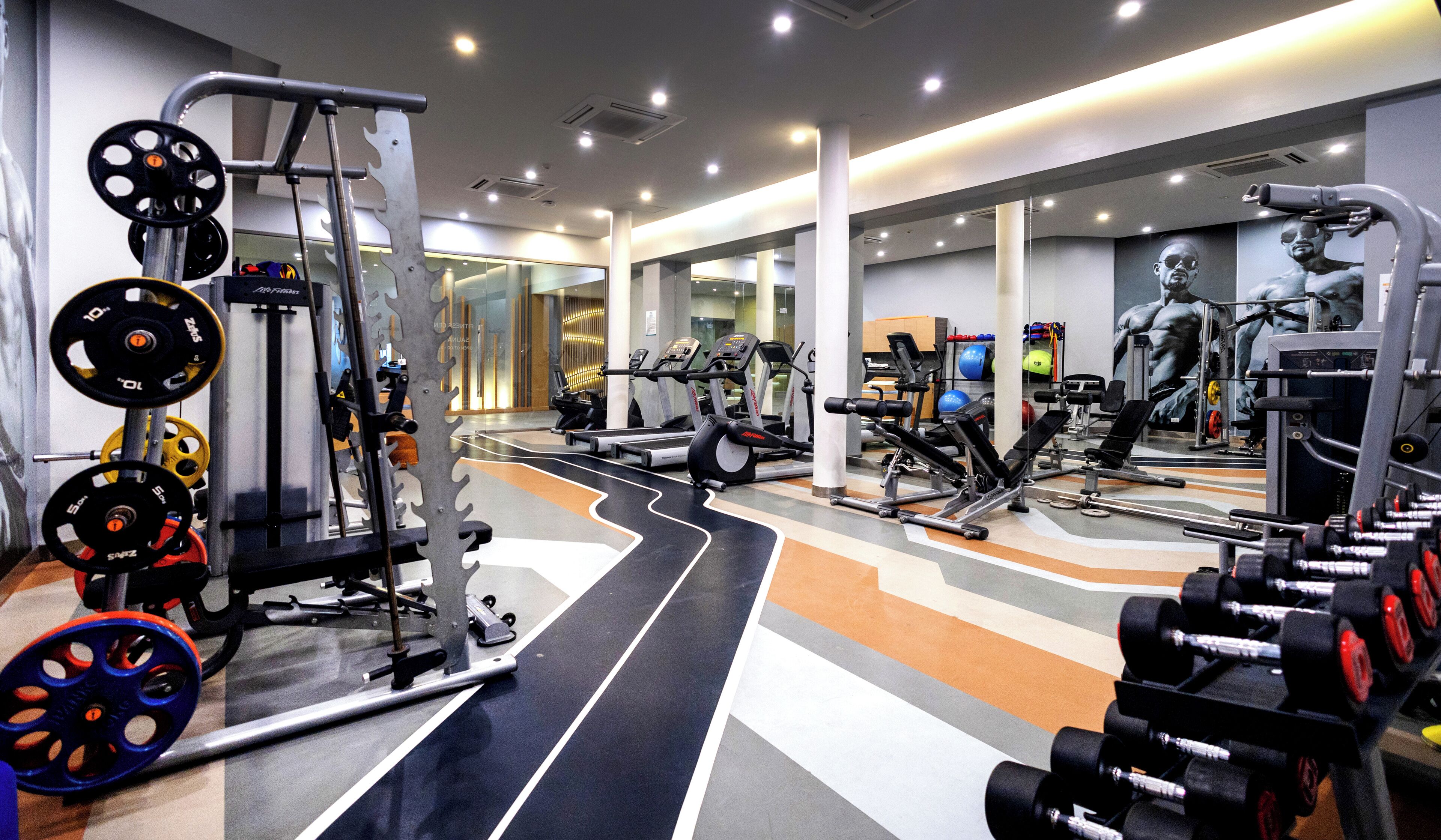 A gym with various exercise equipment, a mirrored wall, and a patterned floor.