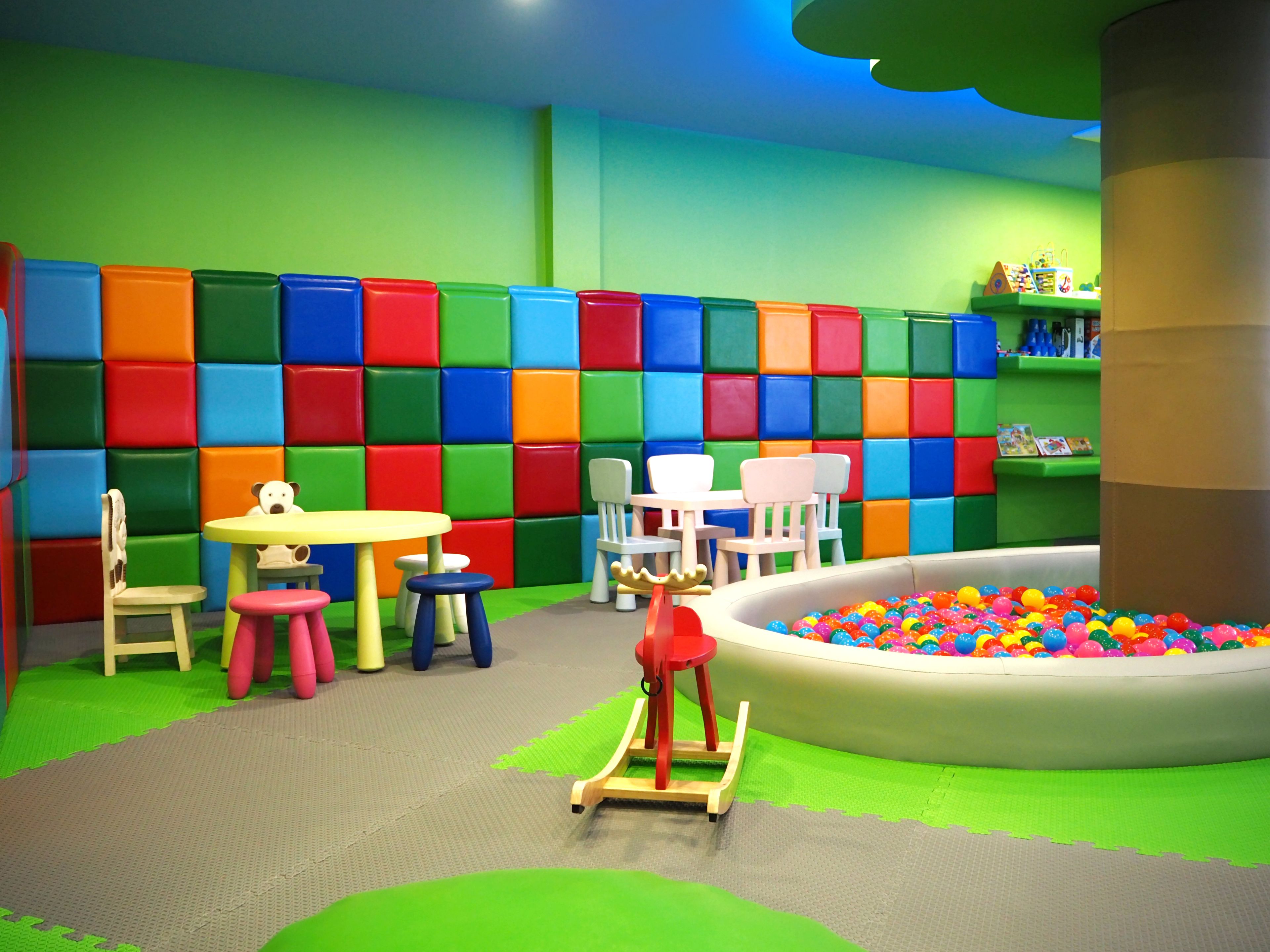 A children's play area with colorful padded walls, a ball pit, and various play furniture.