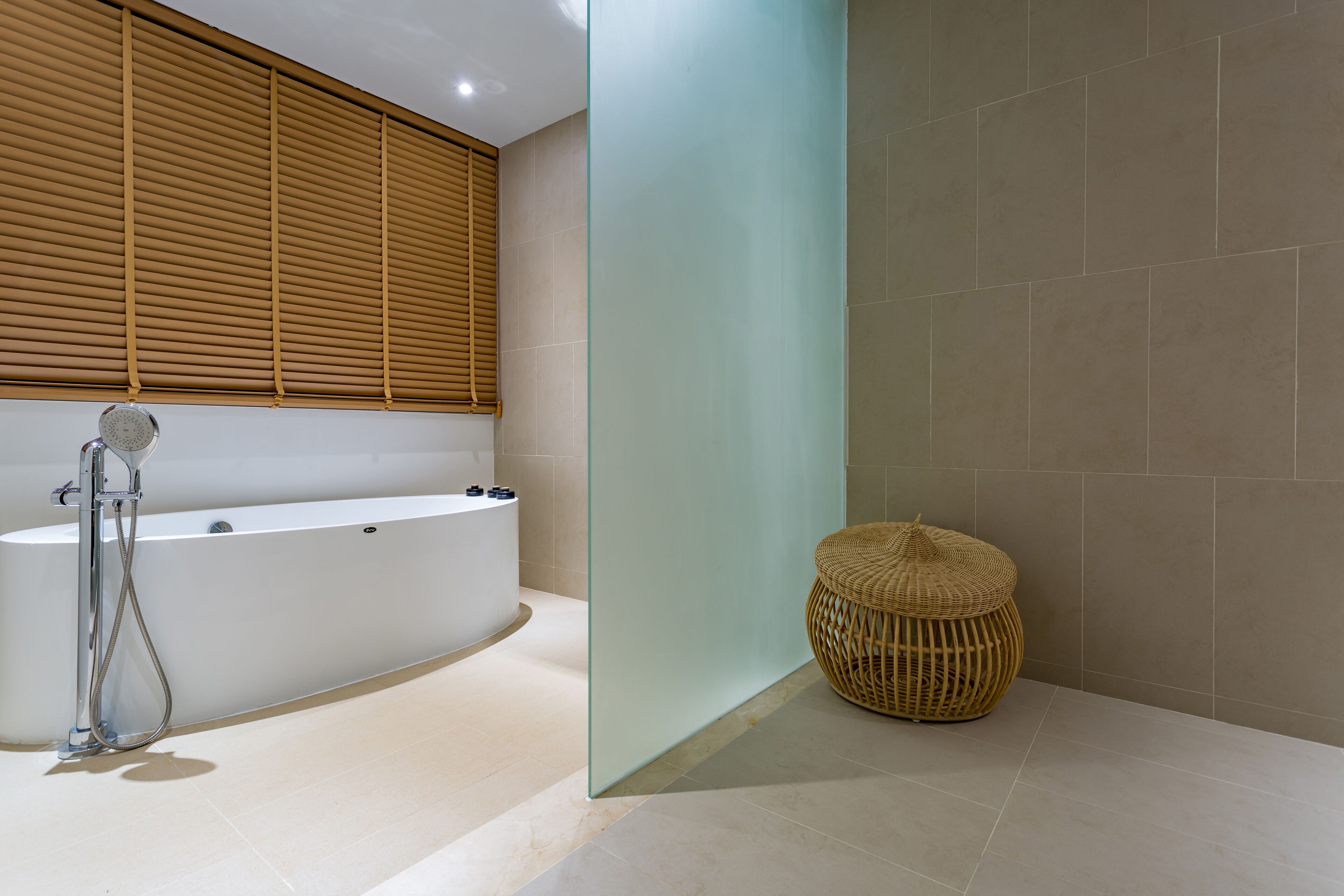 A modern bathroom with a freestanding bathtub, a glass partition, and a woven stool.