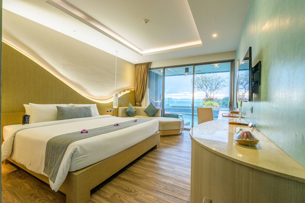 Habitación de hotel moderna con una cama grande, zona de estar y vistas al exterior, además de un mostrador con servicios.