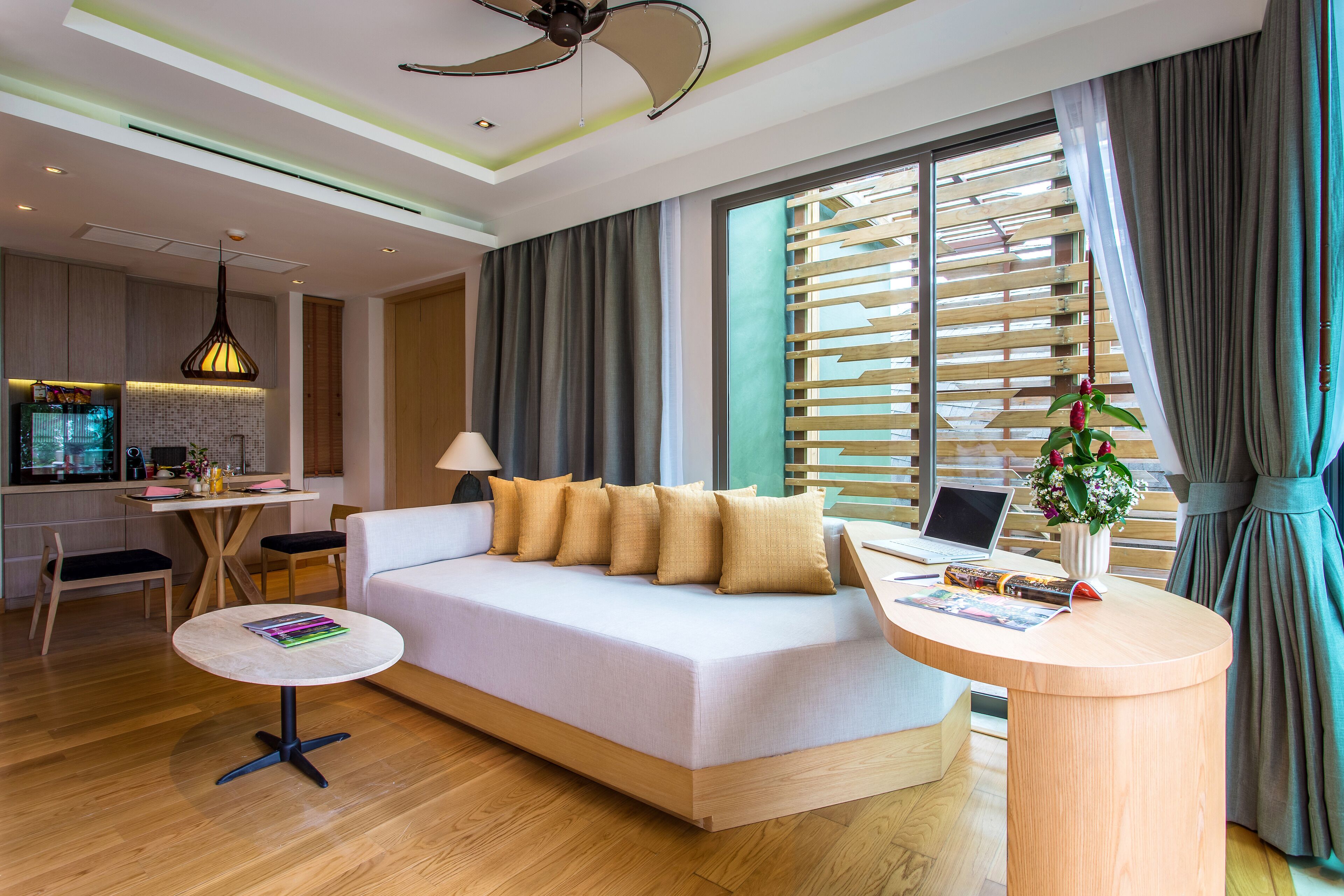 A modern hotel room with a sofa, a round wooden table, a laptop, and a potted plant.