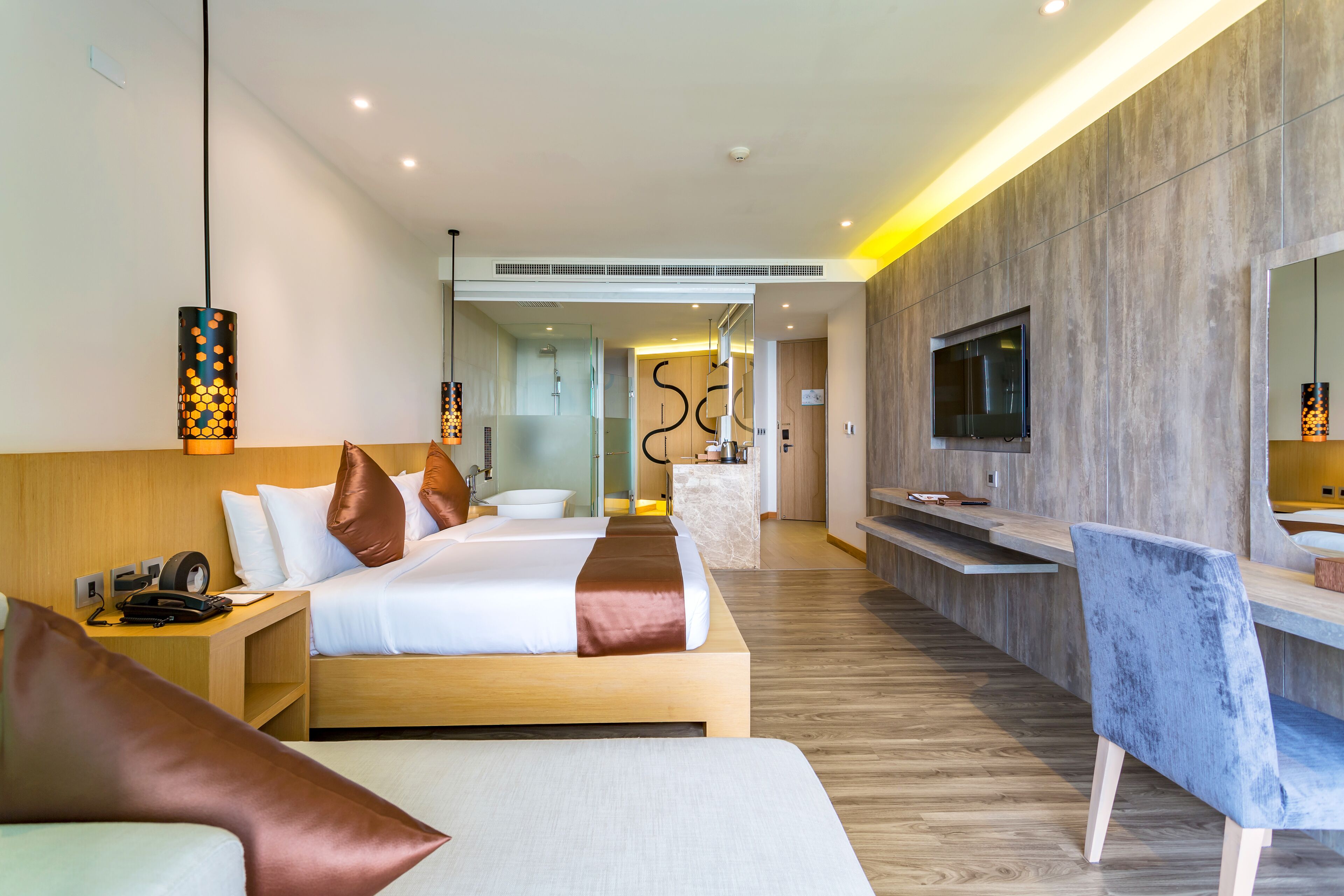 Une chambre d’hôtel moderne dotée d’un grand lit, d’un bureau, d’une télévision et d’une salle de bain visible à travers une porte en verre.