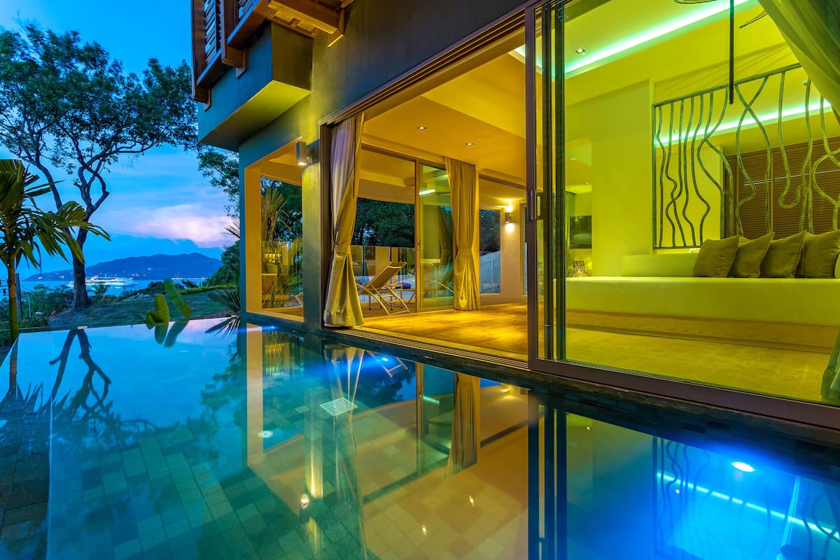 Un hotel moderno con piscina infinita de vidrio, un balcón con sofá y vistas a las montañas.