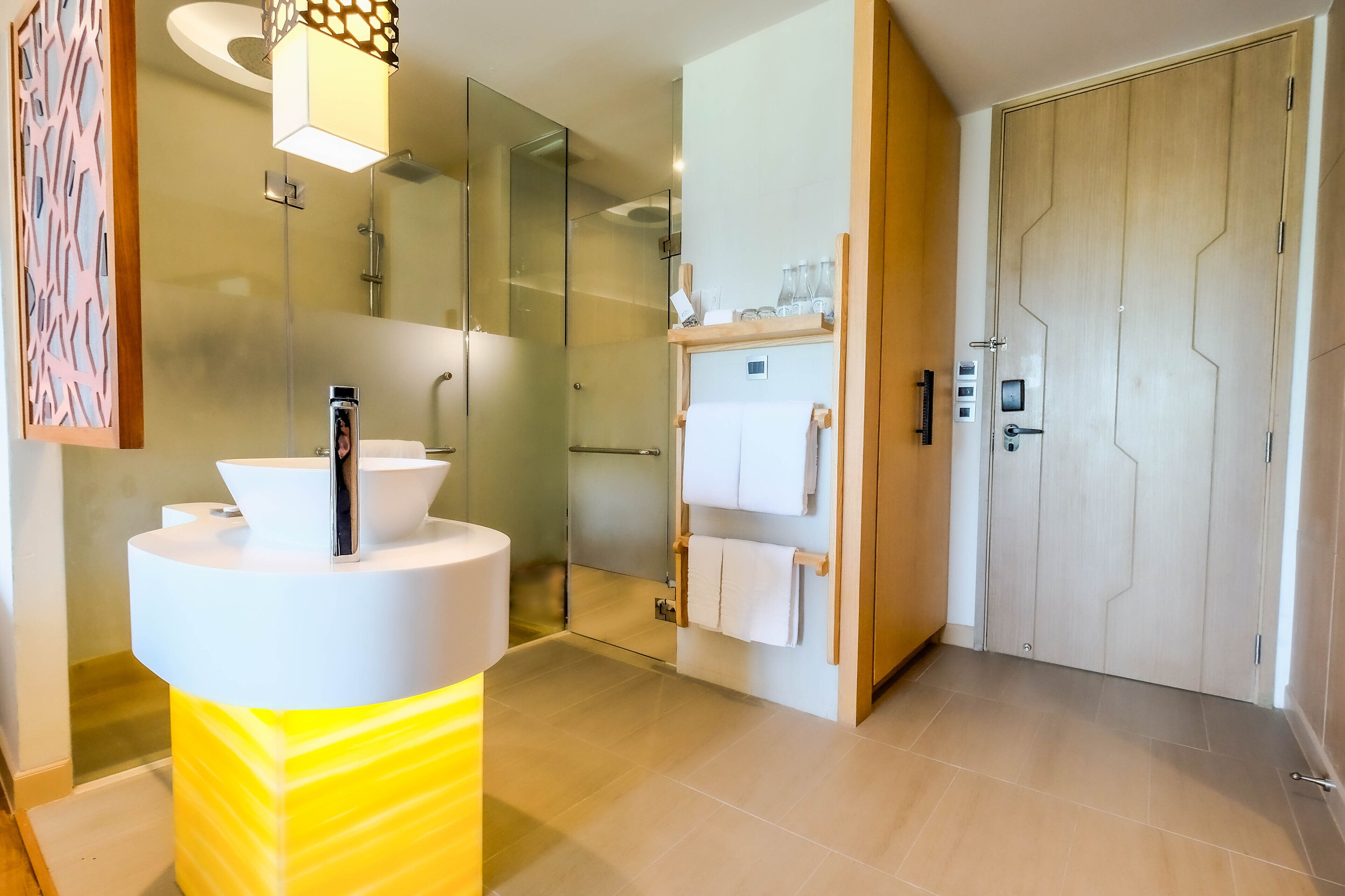 Een moderne badkamer met een douchecabine van glas, een witte wastafel met een gele accentkleur, en een houten deur met een handdoekhouder.