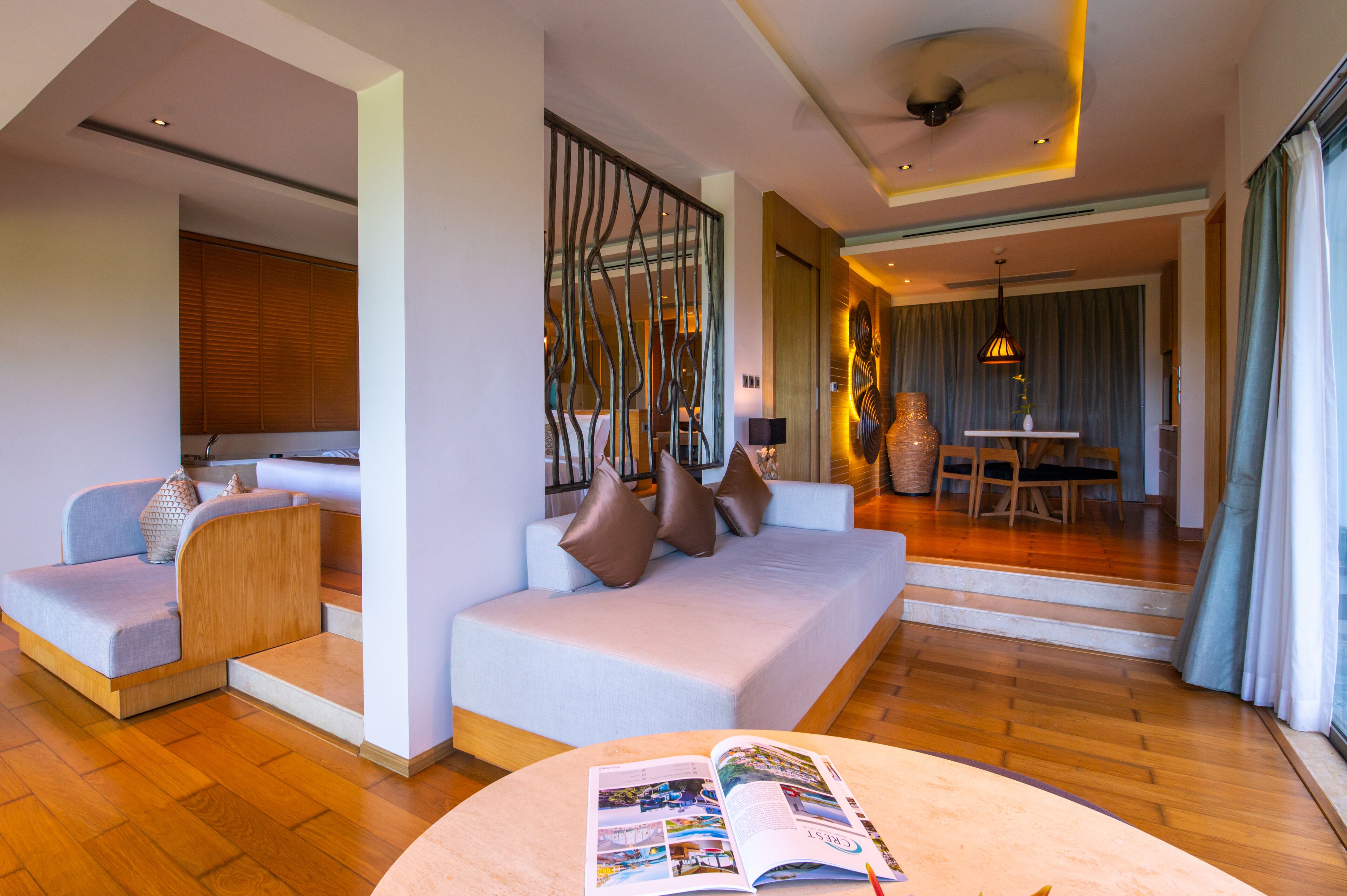 Una habitación de hotel moderna con sofá, zona de comedor y una revista sobre la mesa.