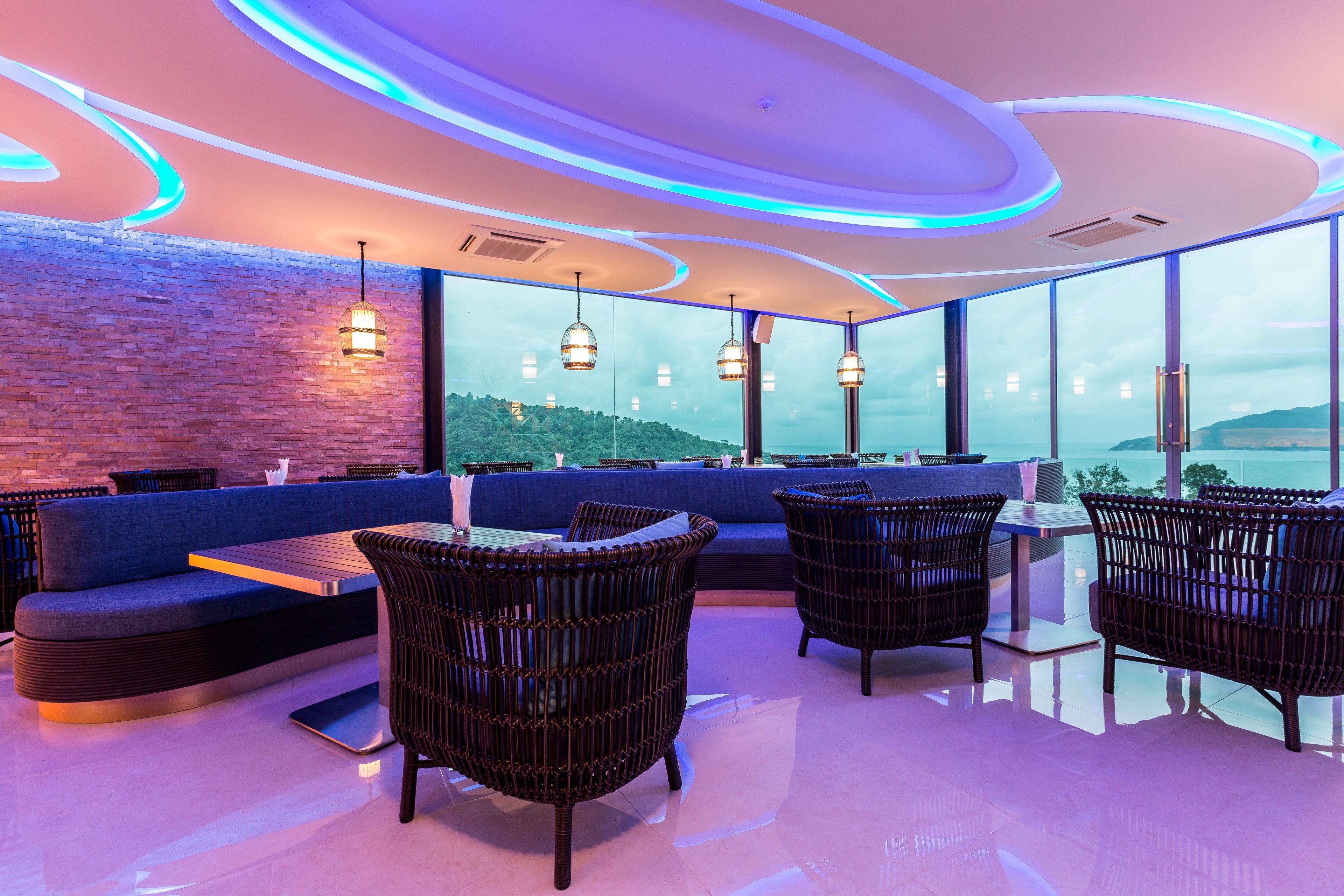 A modern lounge area with a blue sofa, wicker chairs, and pendant lighting.