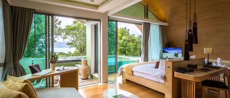 A modern hotel room with a large bed, a desk, a laptop, and a TV. There is a balcony with a view of the outdoors.