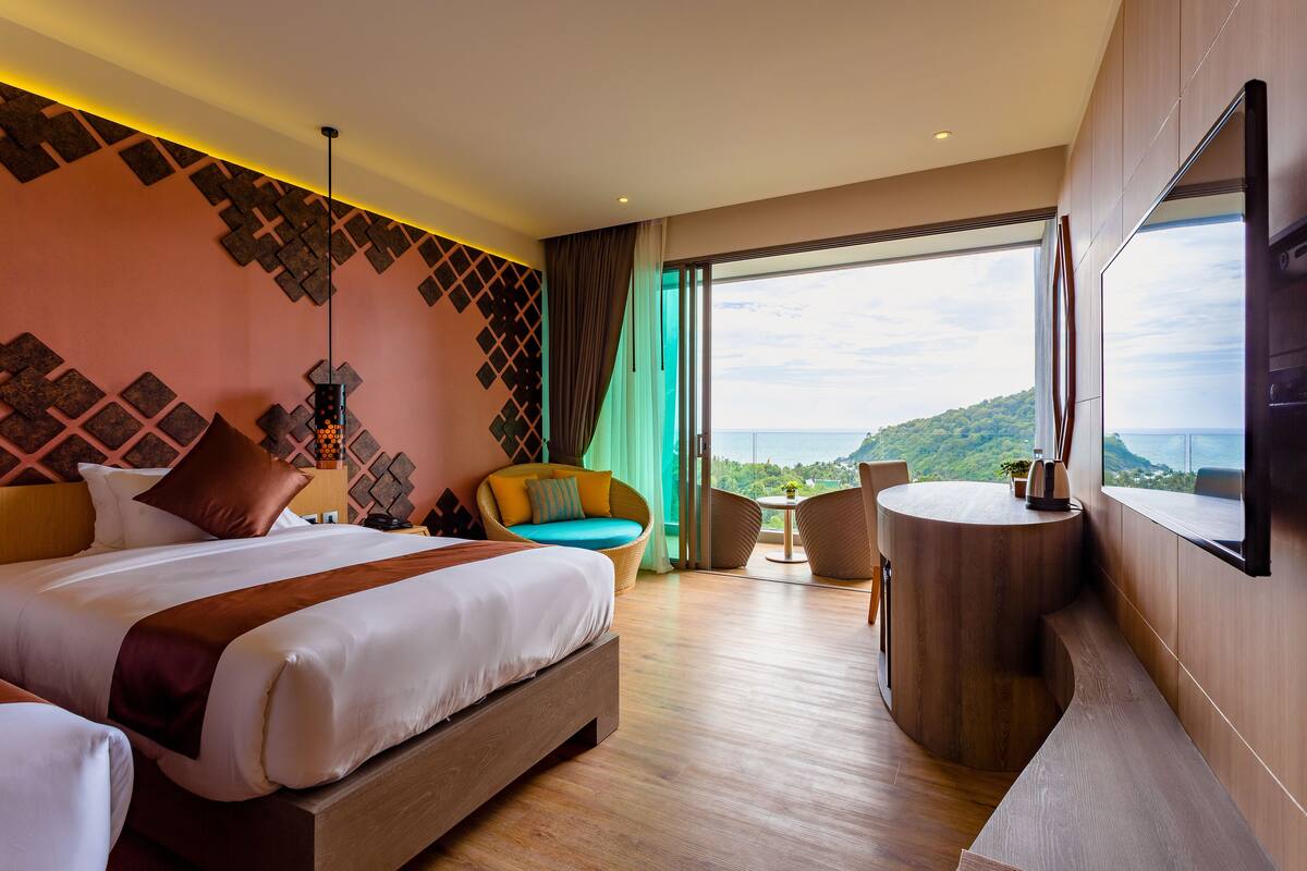 Una habitación de hotel moderna con una cama grande, una mesa redonda de madera, un sillón cómodo y vistas al océano.