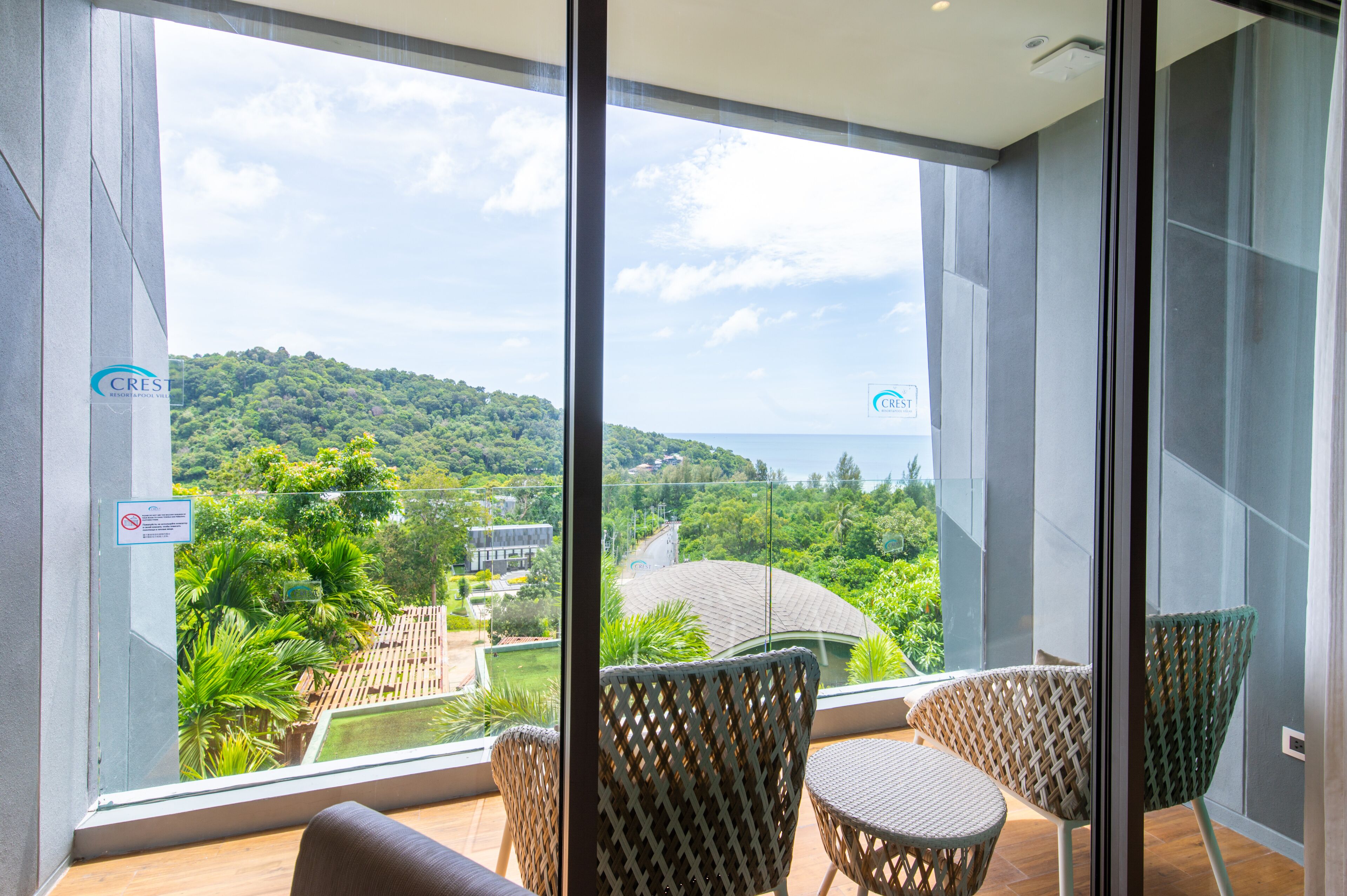 A balcony with wicker chairs and a view of a lush green landscape and the sea.