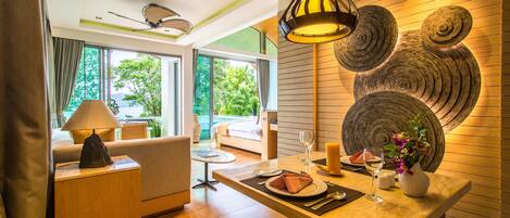A modern hotel room with a dining area, a sofa, and a large window with a view of greenery.