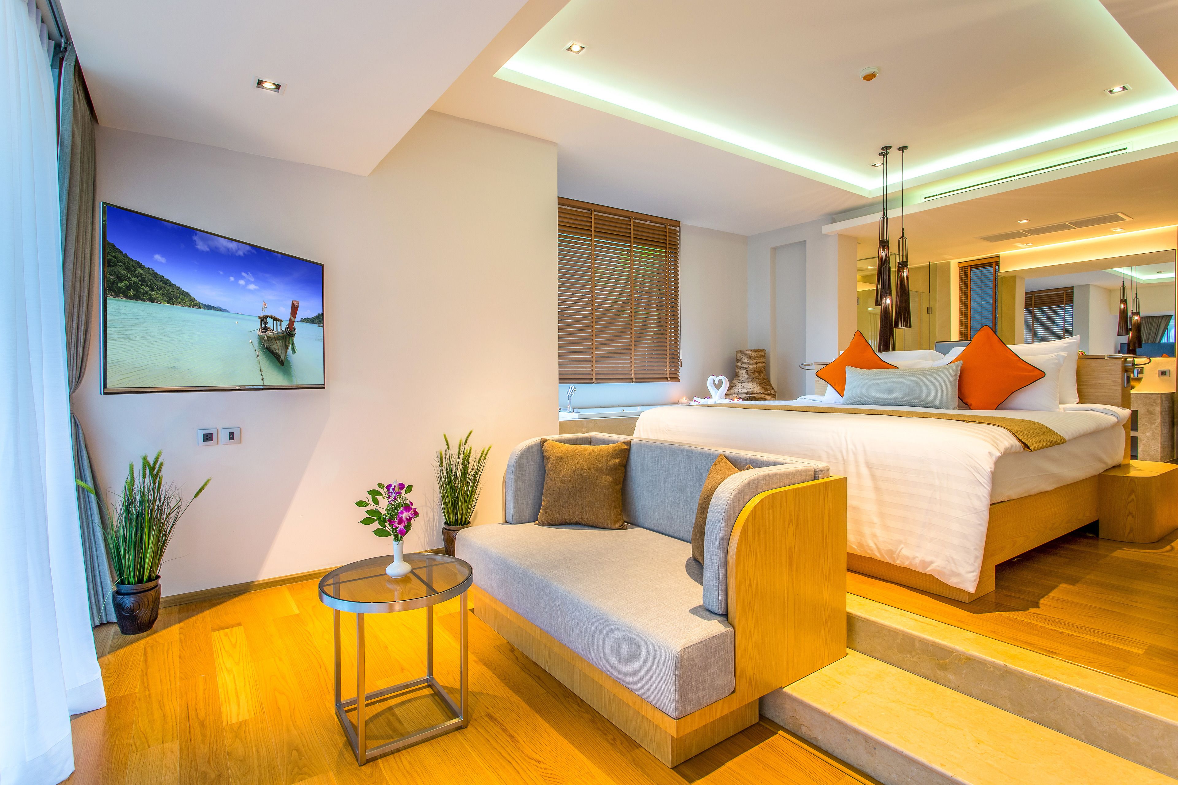 A modern hotel room with a large bed, a sofa, a small table, and a TV displaying a scenic view.