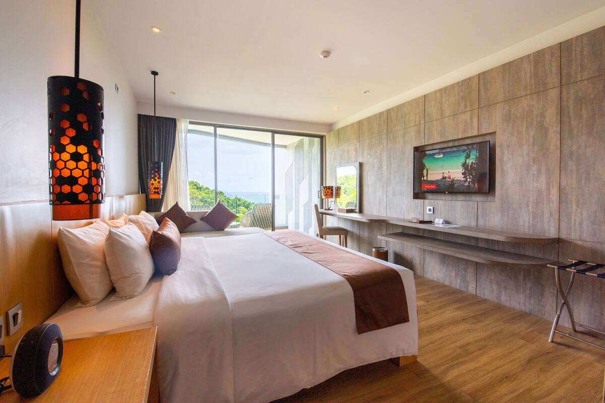 Habitación de hotel moderna con una cama grande, un escritorio, televisión y vistas al exterior.
