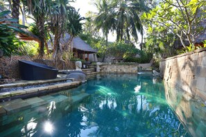 Une piscine aux eaux cristallines, entourée de murs de pierre et d’une végétation tropicale.