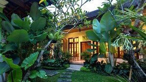 A tropical garden leading to a traditional house with a tiled roof and wooden doors. - The Tunjung Ubud Retreat (Ubud)