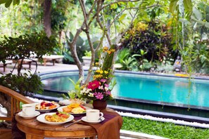 Una mesa con alimentos para el desayuno y un jarrón de flores, con vista a una piscina.