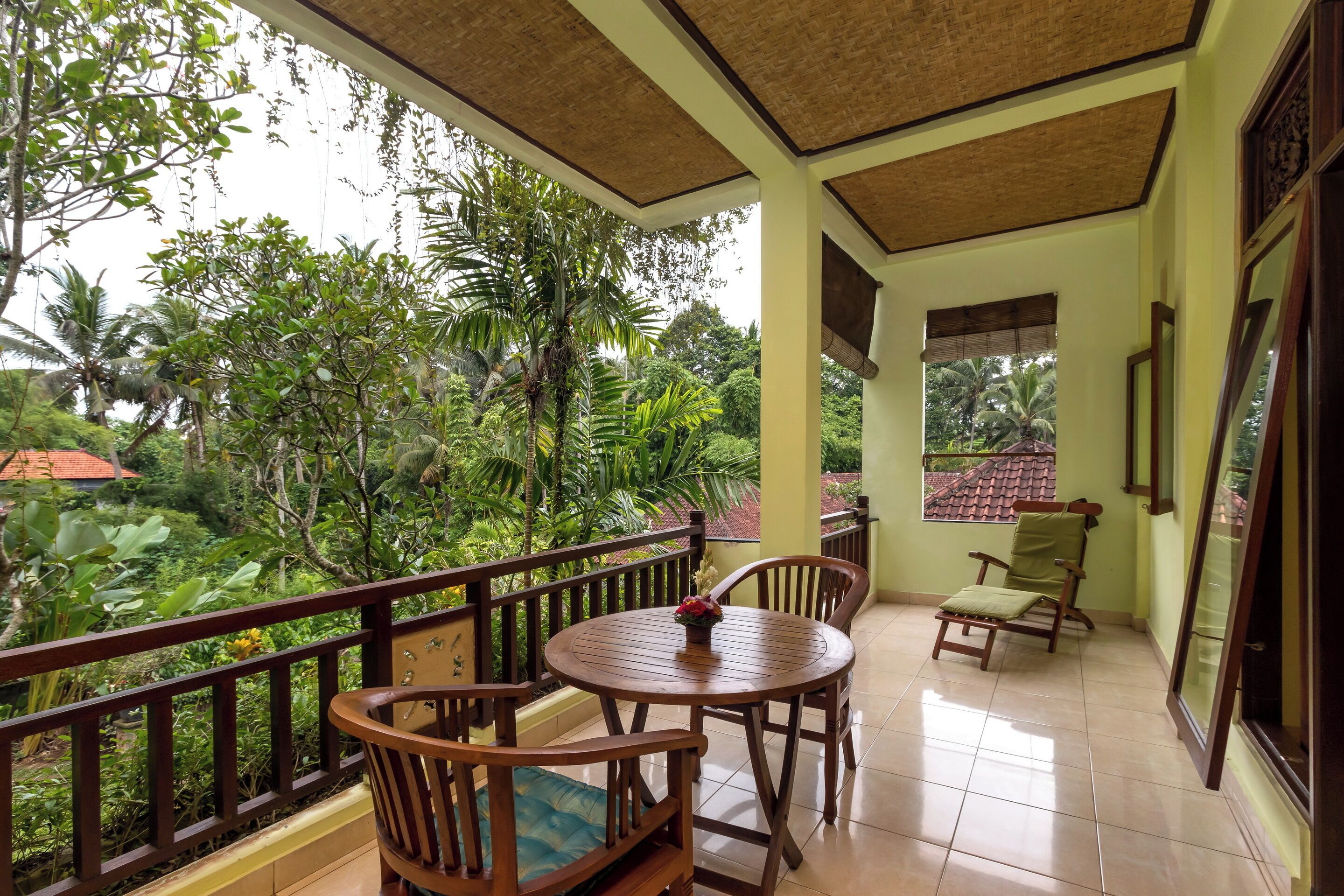 A balcony with wooden furniture, a tiled floor, and a view of lush greenery.