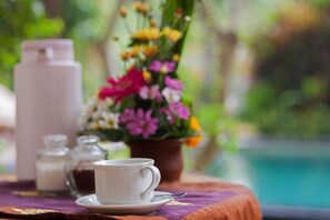 A table with a white cup and saucer, a pink thermos, and a floral arrangement. - The Tunjung Ubud Retreat (Ubud)