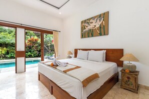 A well-lit bedroom with a large bed, a wooden headboard, a nightstand with a lamp, and a painting on the wall. - The Tunjung Ubud Retreat (Ubud)