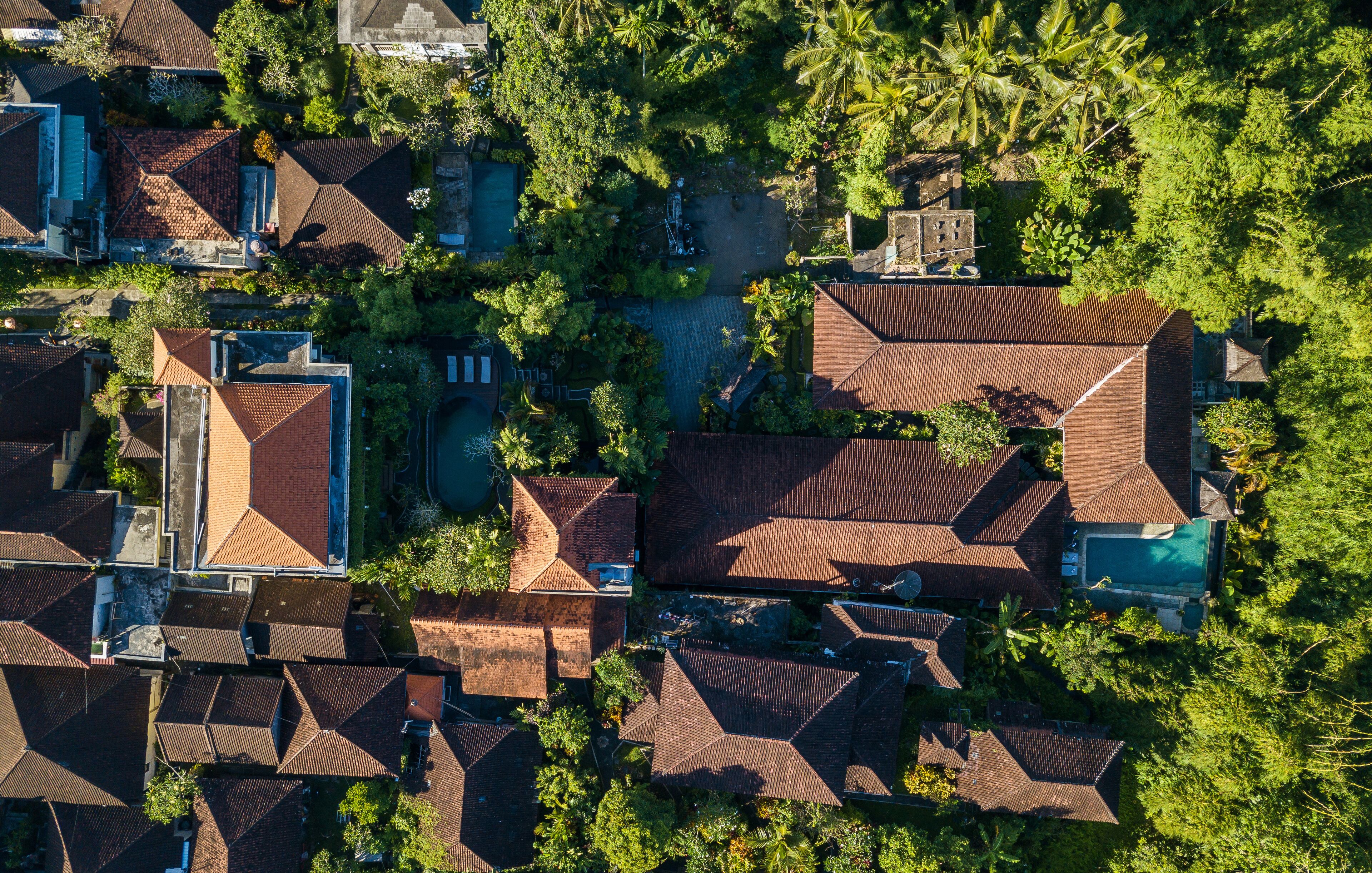 An aerial view of a residential area with multiple houses, each featuring a distinct roof style and surrounded by lush greenery.