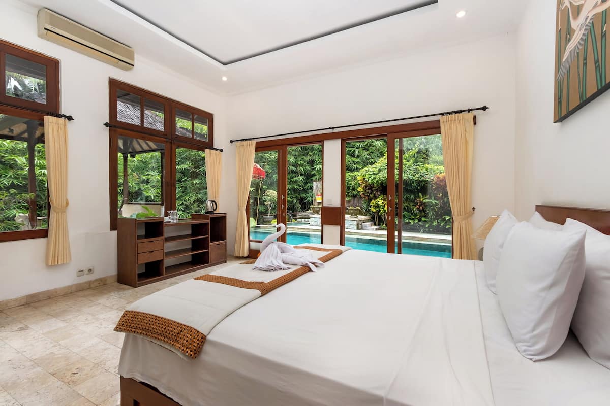 A hotel room with a large bed, a wooden nightstand, a TV, and a view of a swimming pool.