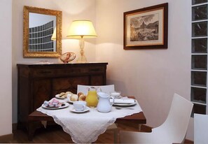 A dining area with a table set for breakfast, a lamp, a mirror, and a framed picture on the wall.