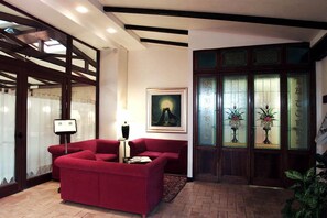 A red sofa in a lobby with a framed painting, a lamp, and a door with frosted glass panels.
